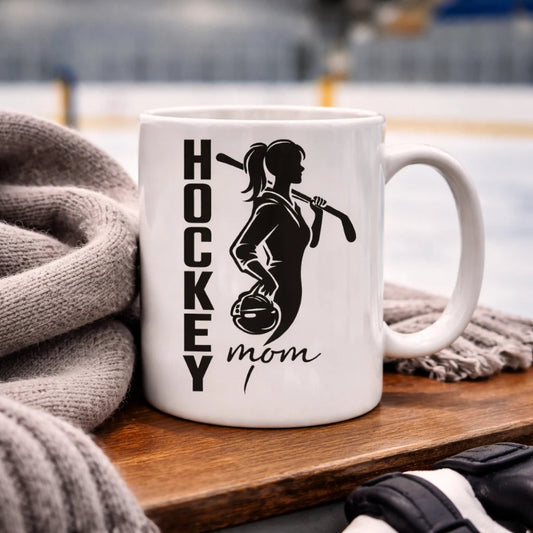Weiße HOCKEY MOM Kaffeetasse mit Eishockey-Mama Motiv neben warmem Wollschal in einer Eishalle